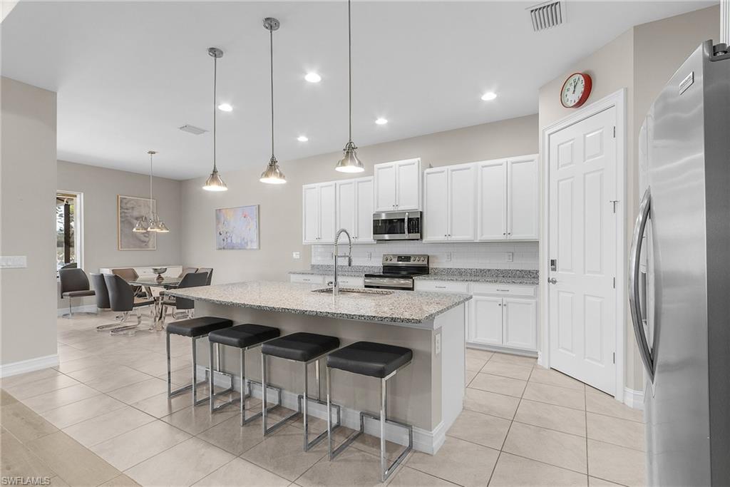 Kitchen with appliances with stainless steel finishes, an island with sink, pendant lighting, light stone counters, and a breakfast bar area
