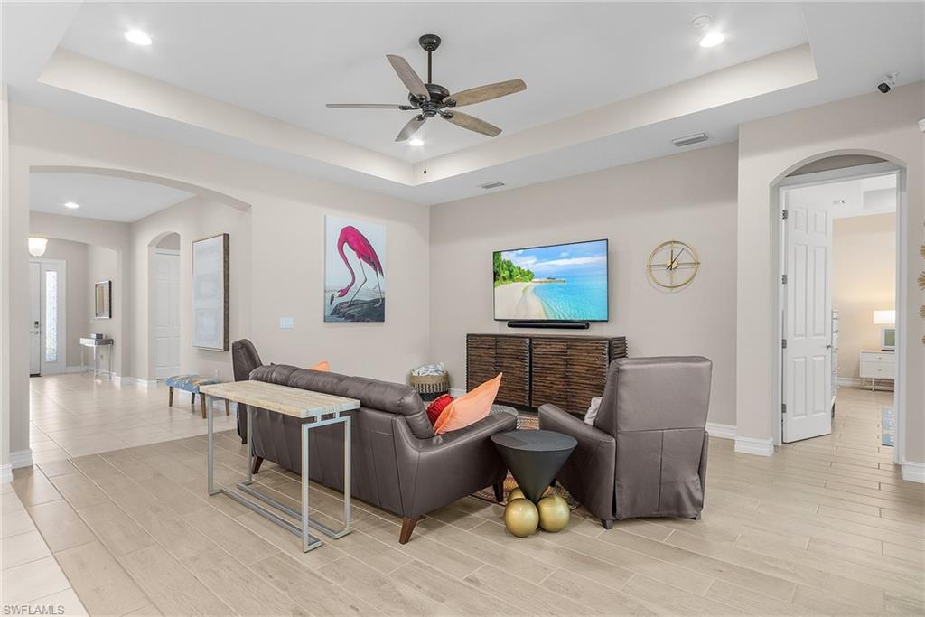 Living room featuring arched walkways, a raised ceiling, a ceiling fan, recessed lighting, and wood finish floors