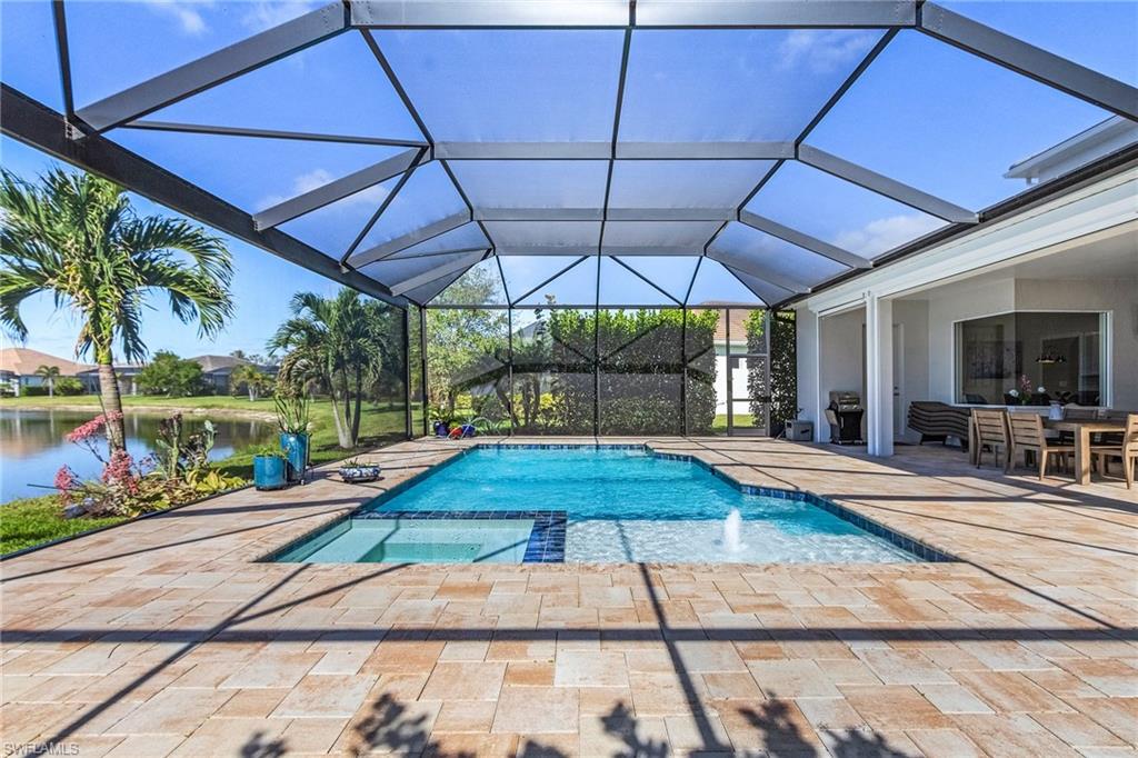 View of swimming pool and hot tub, with a patio area, a pool with connected hot tub, a sunroom, glass enclosure, and a water view