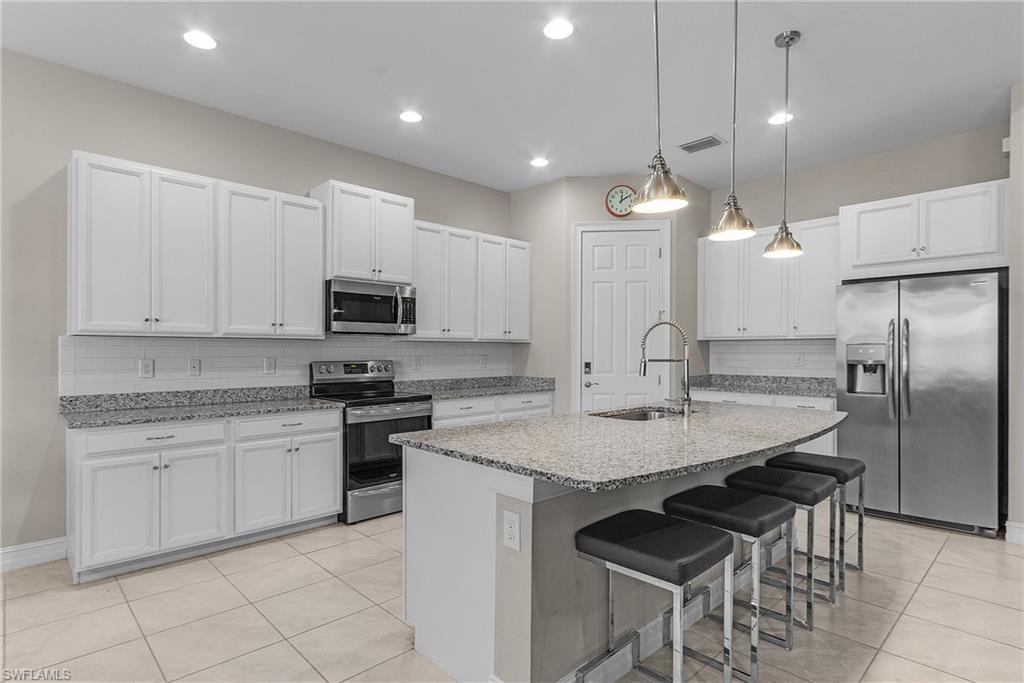 Kitchen with stainless steel appliances, a breakfast bar area, hanging light fixtures, white cabinetry, and light tile patterned floors