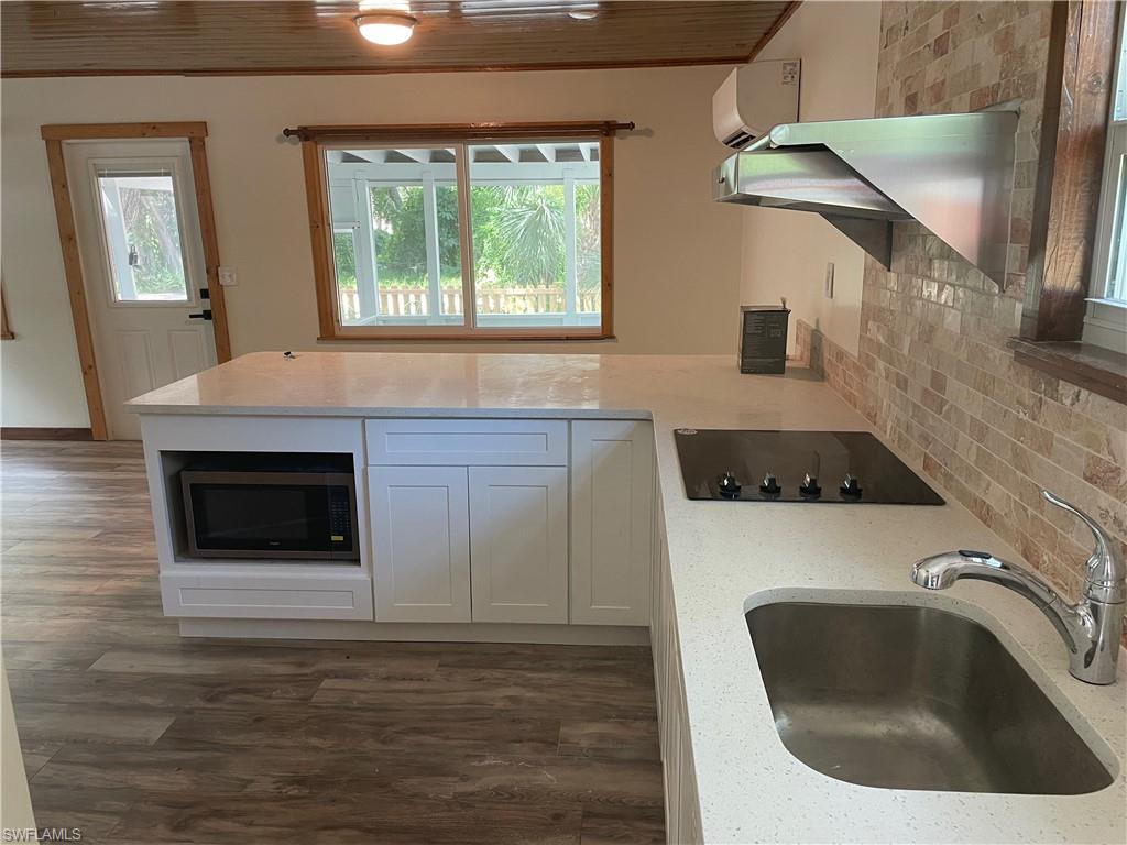 Kitchen featuring white cabinetry, light stone countertops, a peninsula, stainless steel microwave, and crown molding
