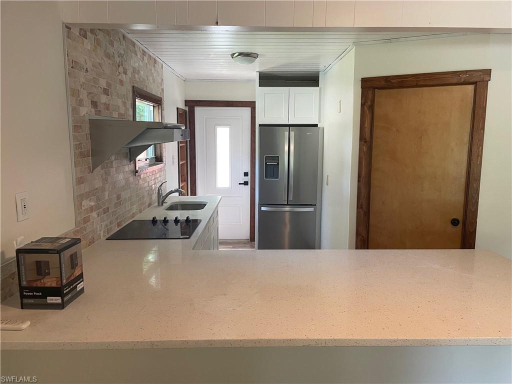 Kitchen featuring stainless steel refrigerator with ice dispenser, white cabinets, a peninsula, black electric cooktop, and light stone countertops