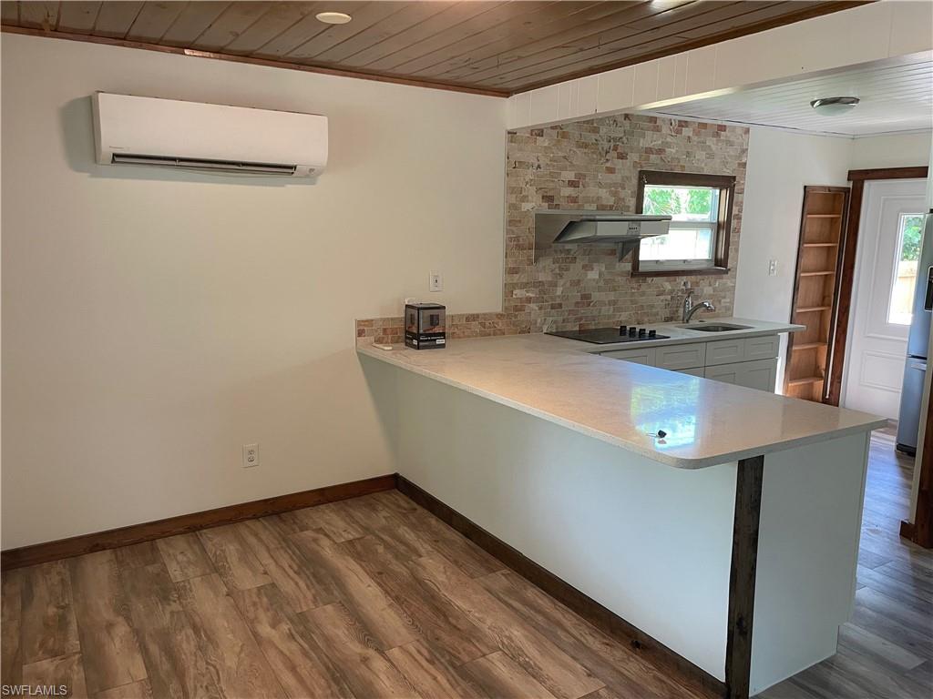 Kitchen with wooden ceiling, a peninsula, dark wood finished floors, a wall mounted air conditioner, and freestanding refrigerator