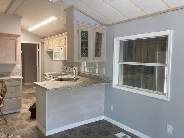 Kitchen with range with electric cooktop, light countertops, white microwave, a peninsula, and glass insert cabinets