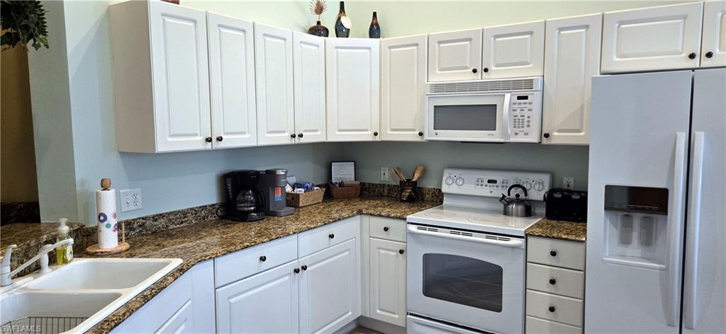 Kitchen with white appliances, white cabinets, and dark stone countertops
