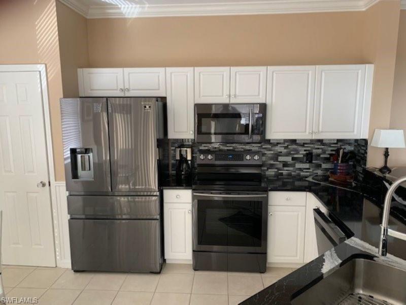 Kitchen featuring stainless steel appliances, white cabinets, ornamental molding, light tile patterned floors, and backsplash