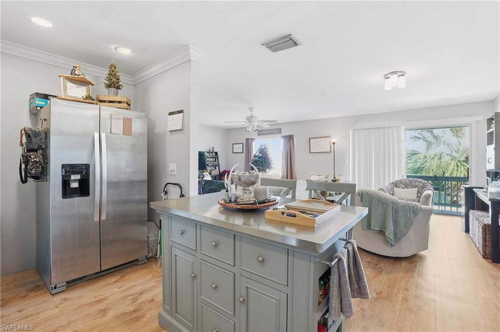 Kitchen featuring open floor plan, stainless steel refrigerator with ice dispenser, a kitchen island, light wood finished floors, and ceiling fan