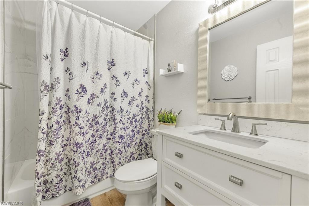Full bath featuring vanity, shower / tub combo, a textured wall, and light wood-style floors