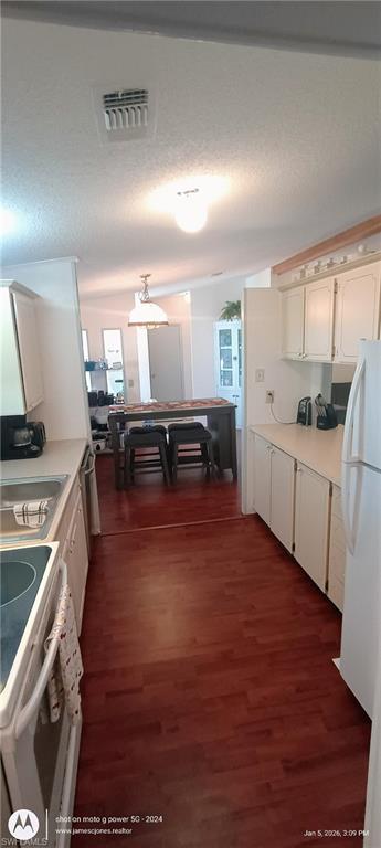 Kitchen with light countertops, white appliances, dark wood-type flooring, a textured ceiling, and decorative light fixtures