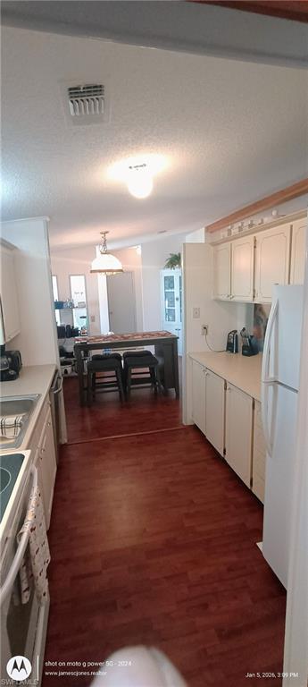 Kitchen with light countertops, white appliances, dark wood-type flooring, a textured ceiling, and decorative light fixtures