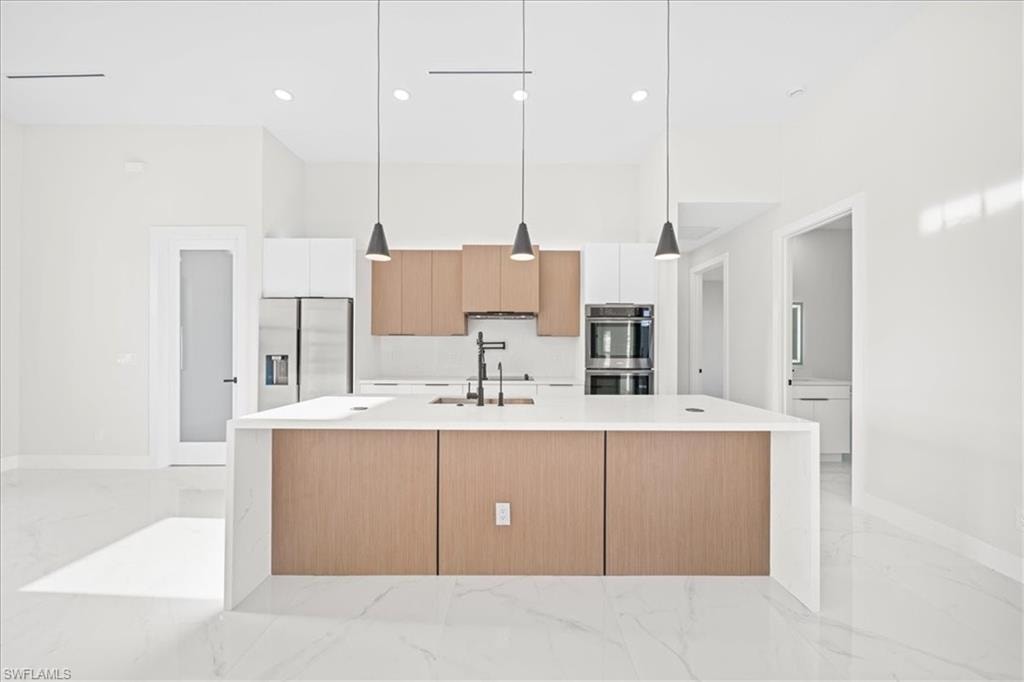 Kitchen with modern cabinets, decorative light fixtures, stainless steel appliances, light stone counters, and dual tone cabinetry