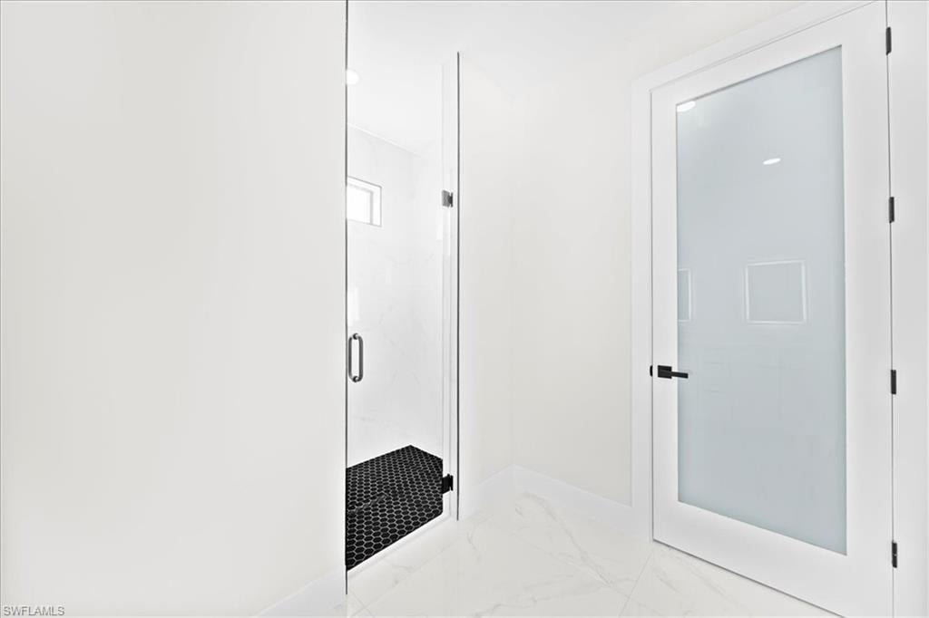 Bathroom featuring a marble finish shower, double vanity, light marble finish floors, and recessed lighting