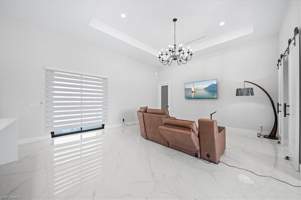 Living area with a barn door, light marble finish flooring, hanging lights, and a raised ceiling