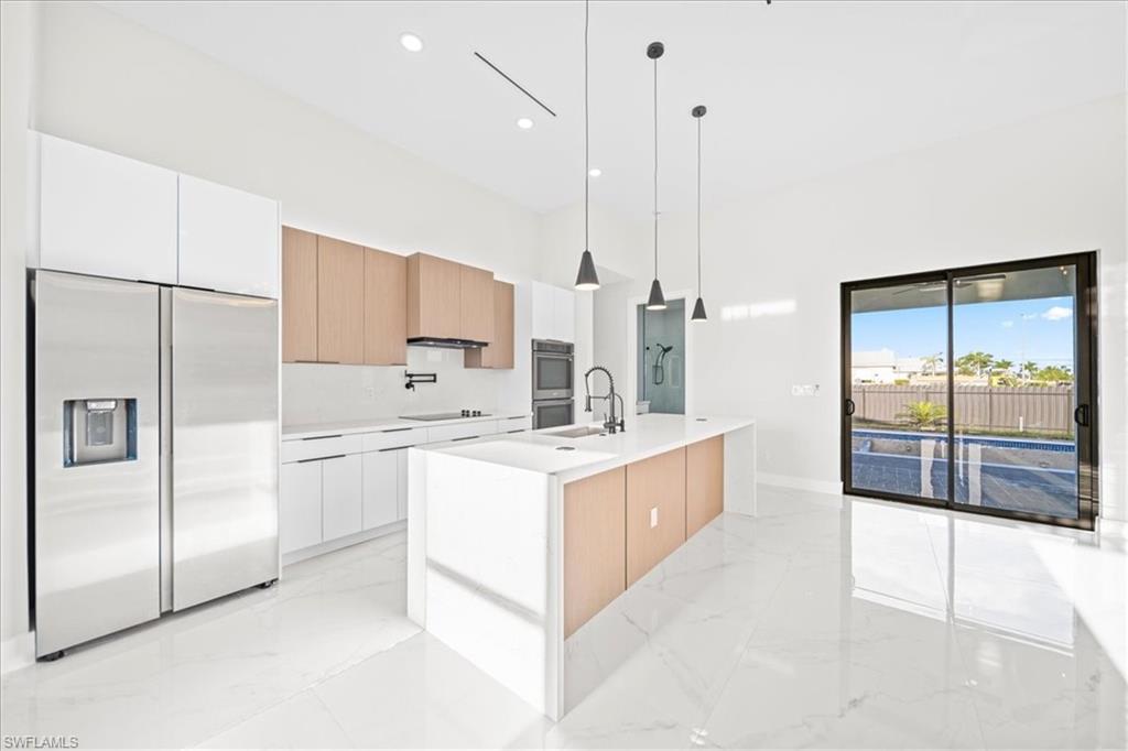 Two tone kitchen with stainless steel appliances, an island with sink, hanging light fixtures, modern cabinets, and two tone cabinetry