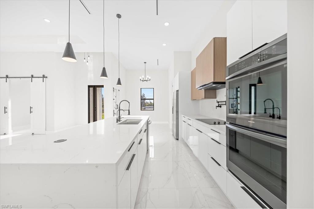 Kitchen with modern cabinets, stainless steel appliances, a large island, light stone countertops, and white cabinets