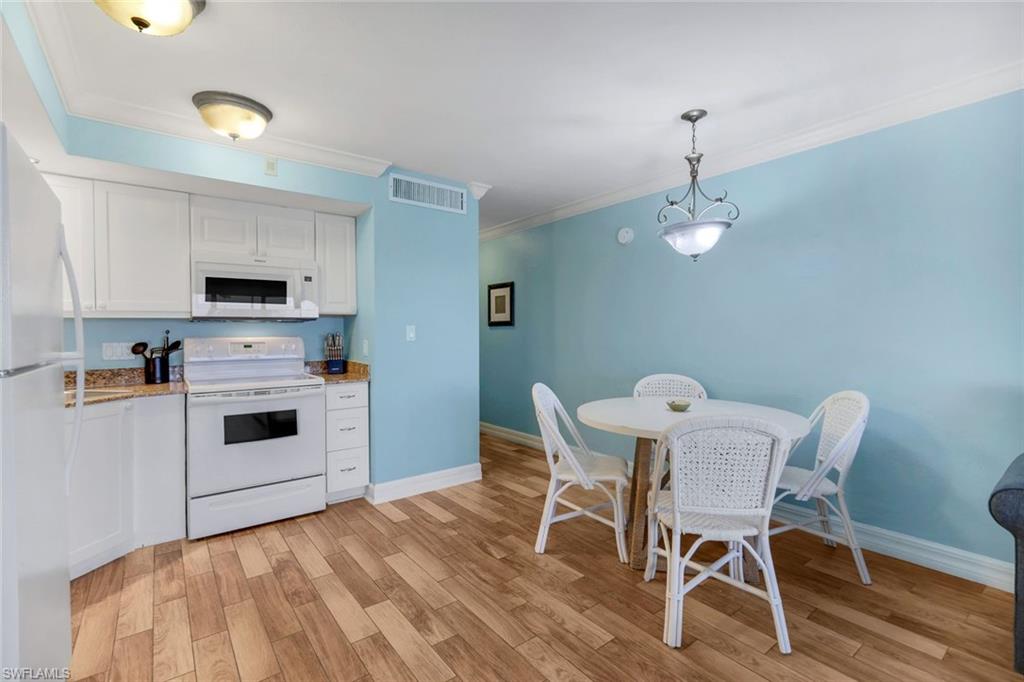 Kitchen with white appliances, decorative light fixtures, light hardwood / wood-style floors, and white cabinets