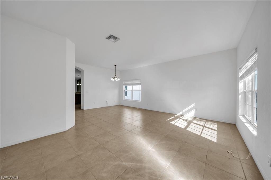 Unfurnished room with arched walkways, a chandelier, and light tile patterned flooring
