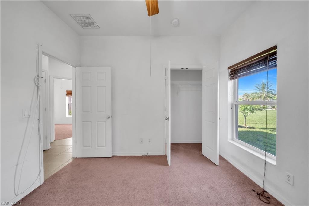 Unfurnished bedroom with light colored carpet, a walk in closet, and ceiling fan