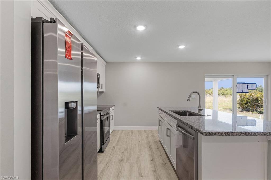 Kitchen with sink, white cabinets, stainless steel appliances, and stone counters