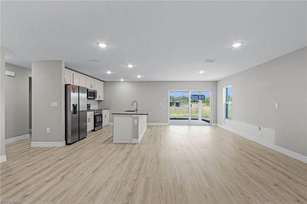 Kitchen with appliances with stainless steel finishes, white cabinetry, and island with sink