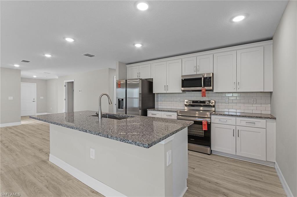 Kitchen with tasteful backsplash, white cabinetry, stainless steel appliances, and granite counters.