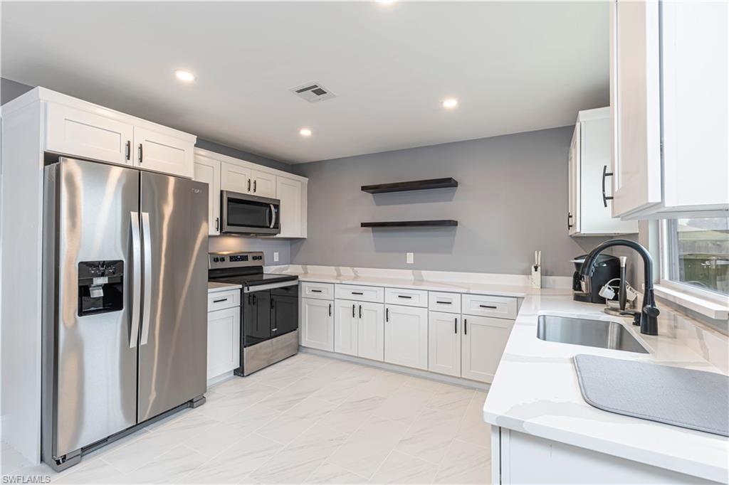 Kitchen with open shelves, appliances with stainless steel finishes, white cabinets, light stone counters, and recessed lighting