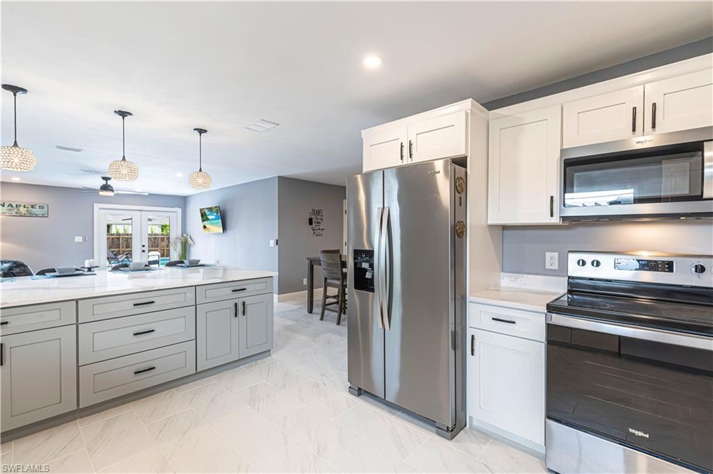 Kitchen with stainless steel appliances, decorative light fixtures, recessed lighting, gray cabinetry, and light stone counters
