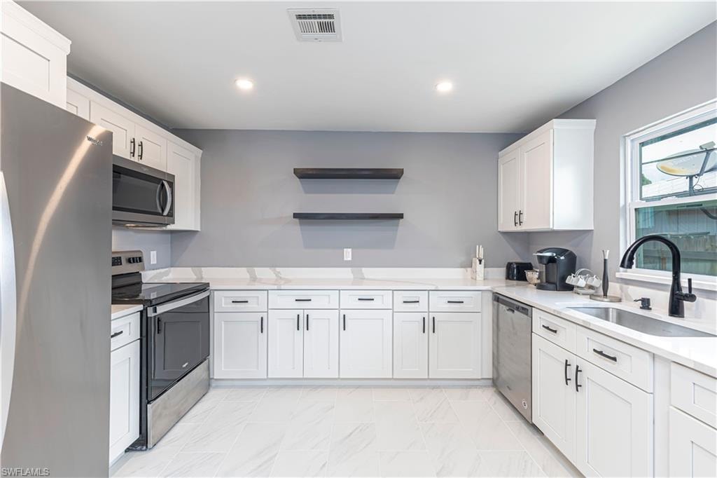 Kitchen with stainless steel appliances, white cabinetry, open shelves, light stone counters, and recessed lighting