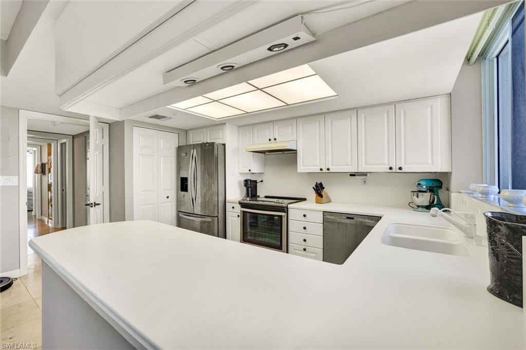 Kitchen with visible vents, a sink, a peninsula, under cabinet range hood, and stainless steel appliances