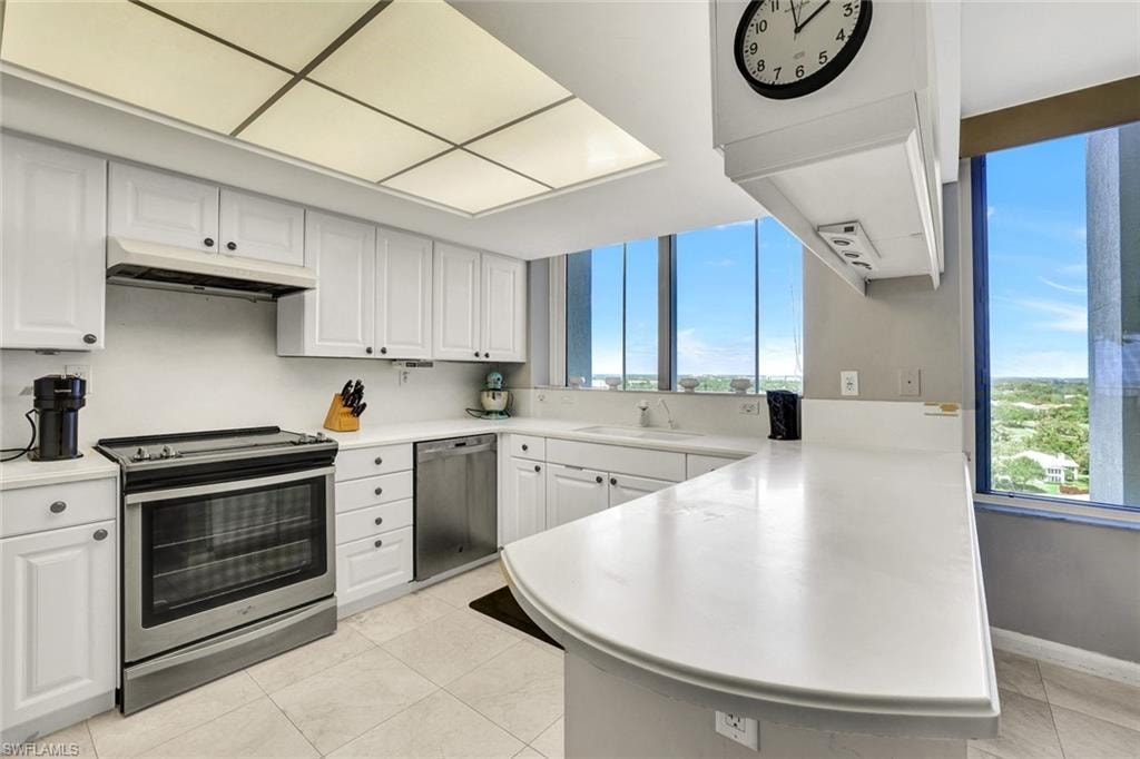 Kitchen featuring a sink, appliances with stainless steel finishes, a peninsula, under cabinet range hood, and white cabinetry
