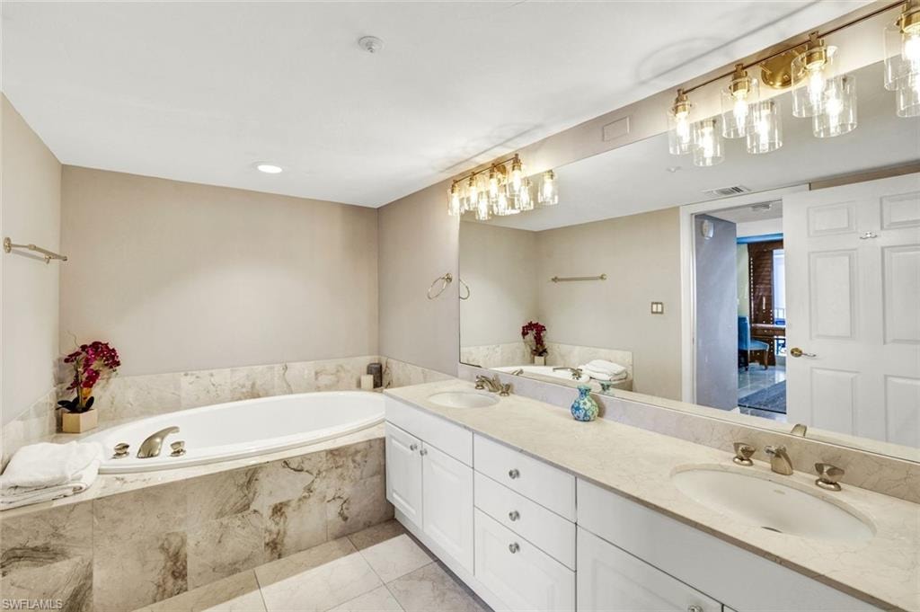 Full bathroom with double vanity, a bath, visible vents, and a sink