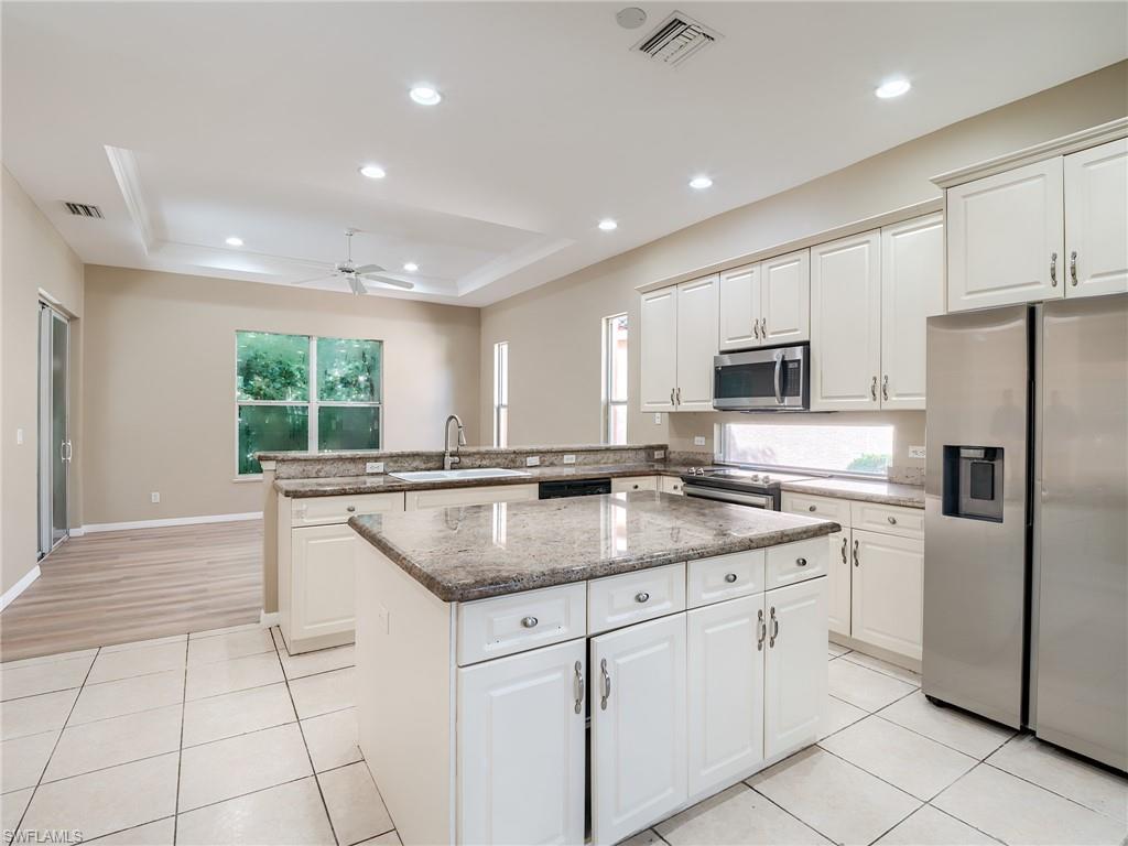 Kitchen featuring white cabinets, appliances with stainless steel finishes, light stone countertops, ceiling fan, and a tray ceiling