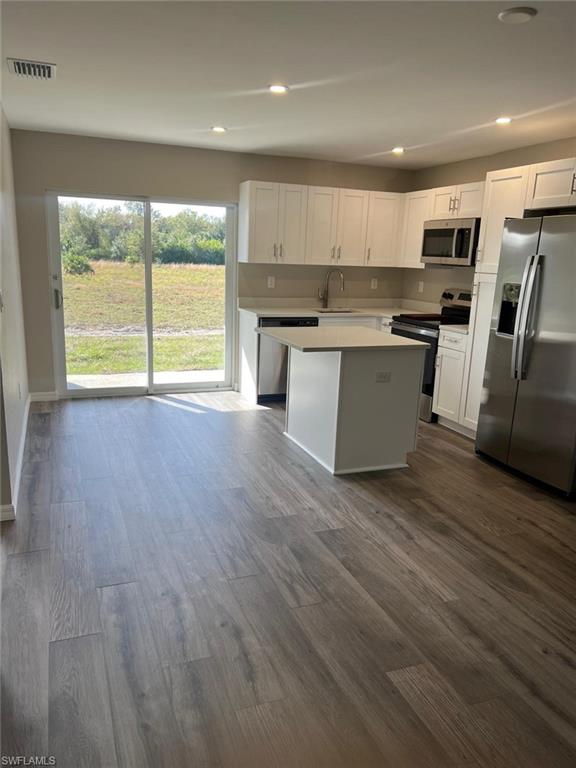 Kitchen featuring appliances with stainless steel finishes, recessed lighting, white cabinetry, a kitchen island, and dark wood-style floors