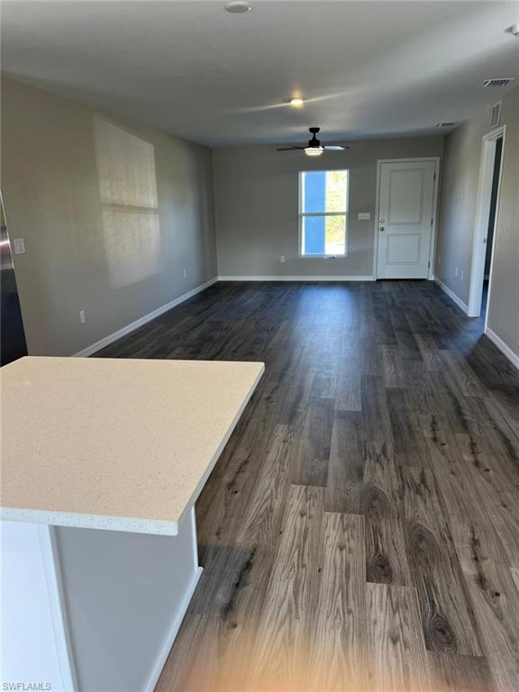 Unfurnished living room featuring dark wood-type flooring and ceiling fan