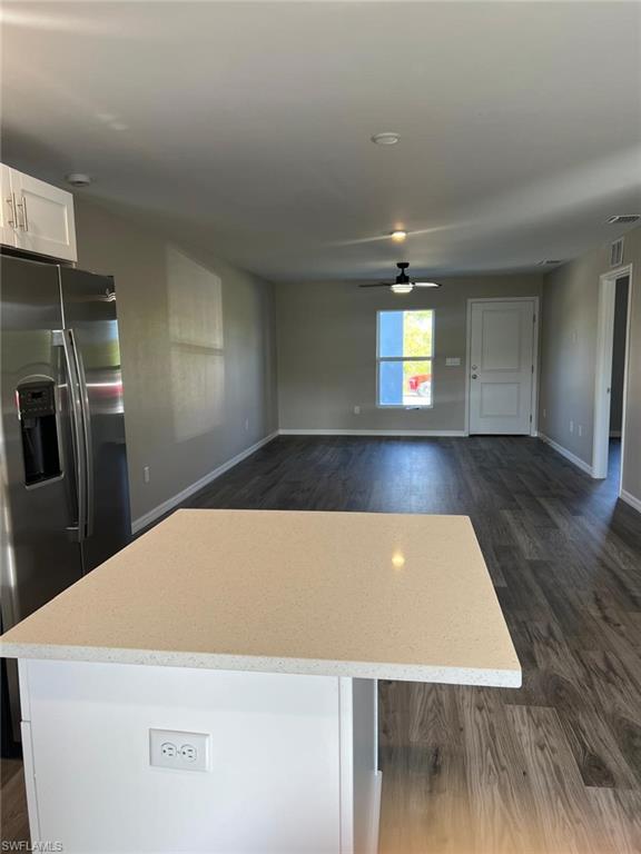 Kitchen with stainless steel fridge with ice dispenser, white cabinetry, open floor plan, dark wood finished floors, and light stone counters