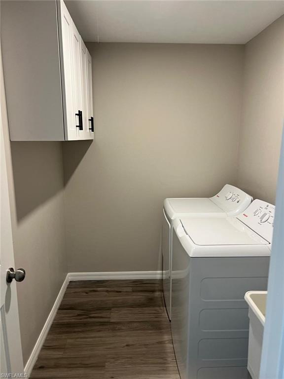 Laundry area featuring dark wood-style flooring, separate washer and dryer, and cabinet space