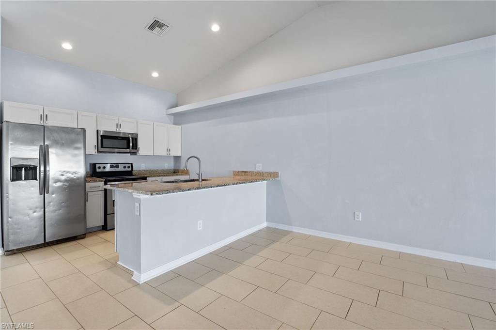 Kitchen featuring appliances with stainless steel finishes, white cabinets, a peninsula, recessed lighting, and dark stone counters