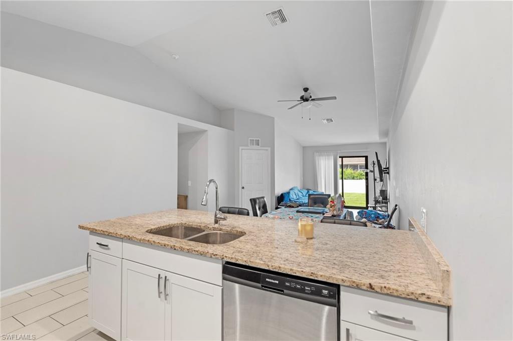 Kitchen with dishwasher, white cabinets, vaulted ceiling, light stone counters, and a peninsula