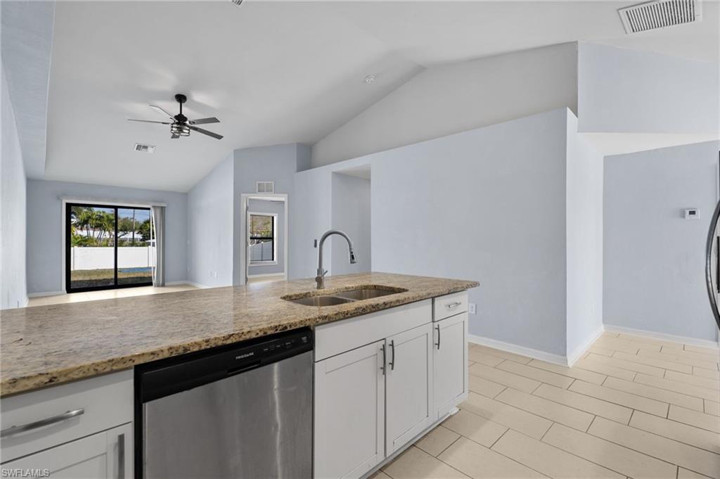 Kitchen with lofted ceiling, dishwasher, light stone countertops, white cabinetry, and a ceiling fan
