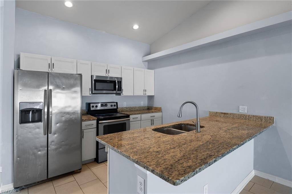 Kitchen featuring appliances with stainless steel finishes, white cabinets, dark stone countertops, light tile patterned floors, and recessed lighting