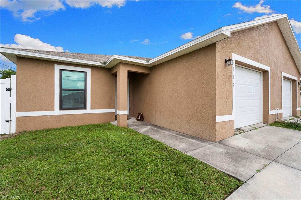 Ranch-style house featuring stucco siding, a front lawn, an attached garage, and a gate