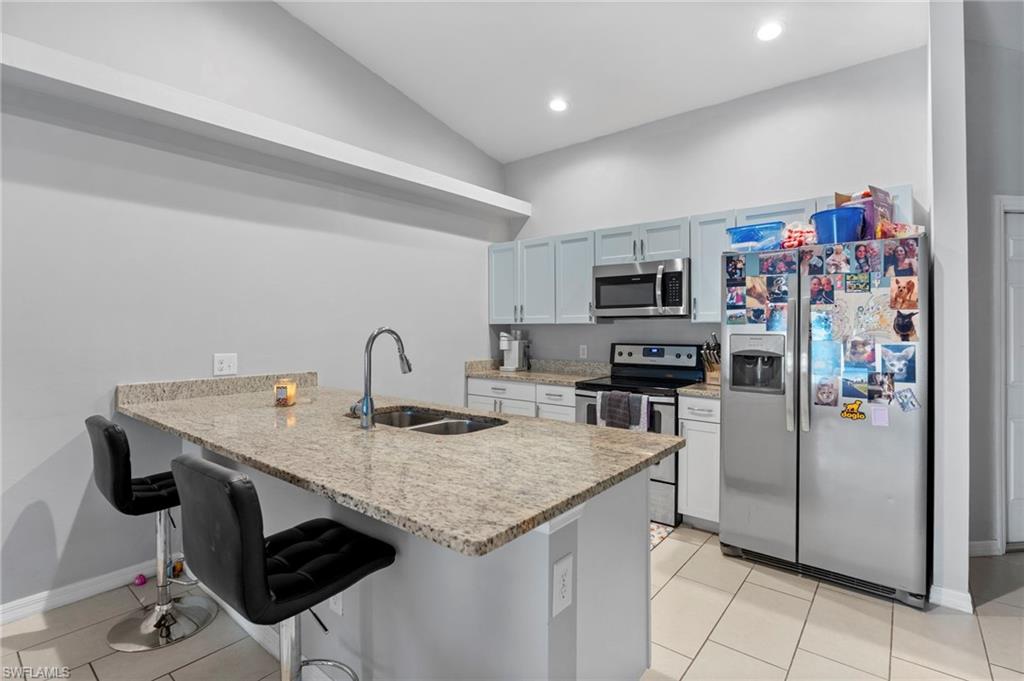 Kitchen with stainless steel appliances, a breakfast bar area, a peninsula, light tile patterned floors, and recessed lighting