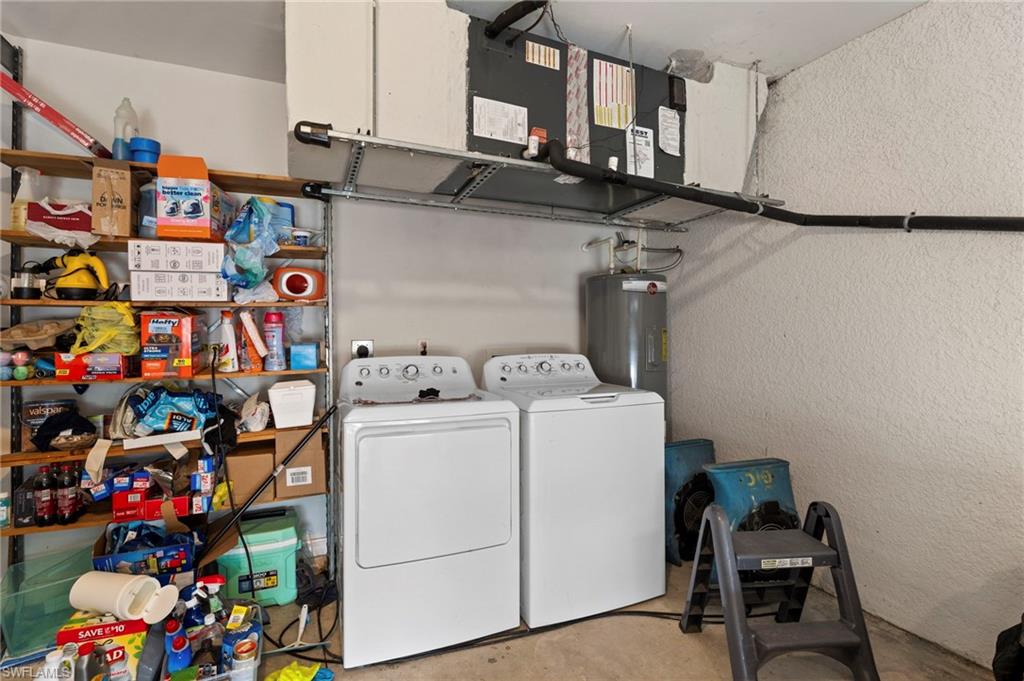 Laundry area with a textured wall, concrete floors, washing machine and clothes dryer, and electric water heater