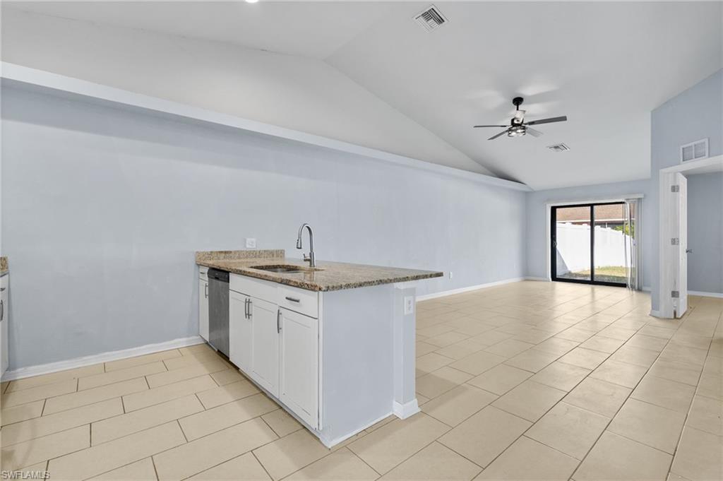 Kitchen with a peninsula, white cabinets, lofted ceiling, open floor plan, and light stone counters