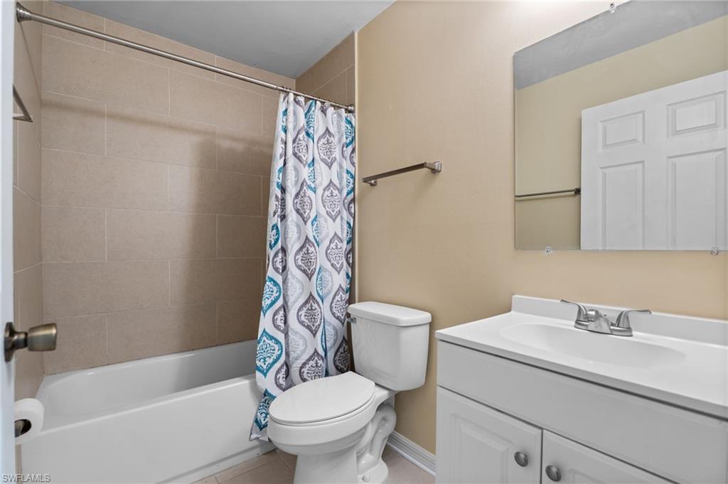 Full bath featuring vanity, shower / bath combo with shower curtain, and light tile patterned flooring