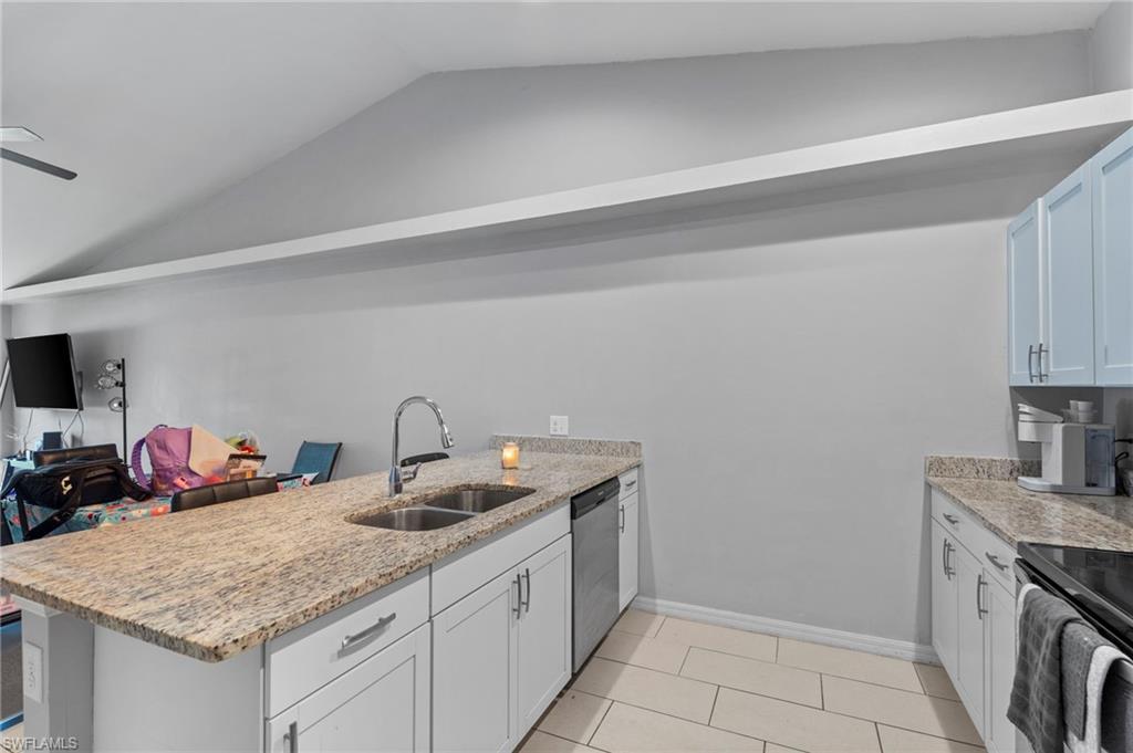 Kitchen featuring a peninsula, light stone counters, lofted ceiling, and white cabinetry