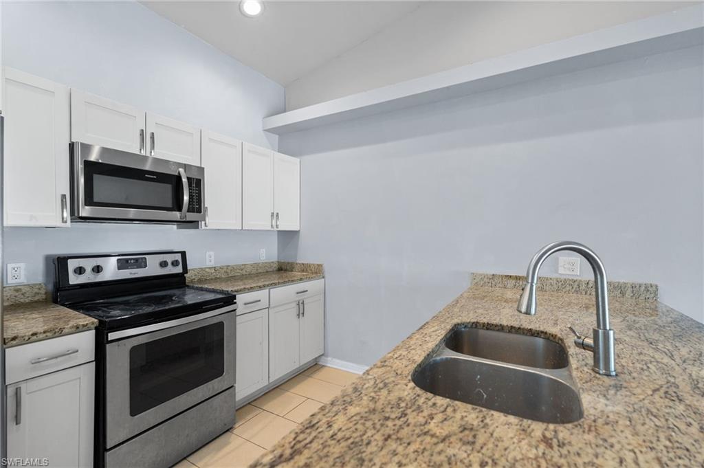 Kitchen with stainless steel appliances, white cabinetry, light stone countertops, and light tile patterned floors