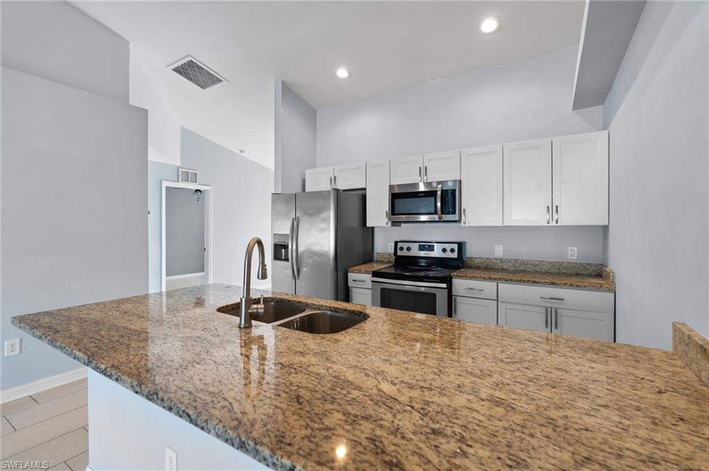 Kitchen featuring dark stone counters, appliances with stainless steel finishes, white cabinets, a peninsula, and recessed lighting