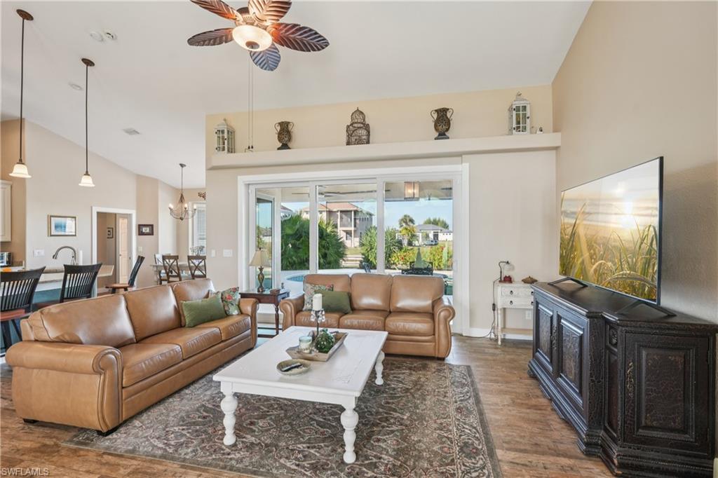 Living area featuring dark wood-style flooring, ceiling fan, high vaulted ceiling, a wood stove, and a chandelier