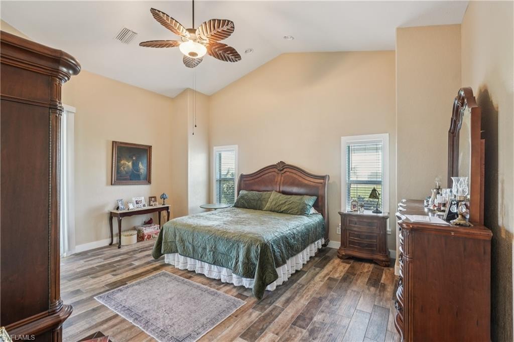 Bedroom with high vaulted ceiling, dark wood-type flooring, multiple windows, and a ceiling fan